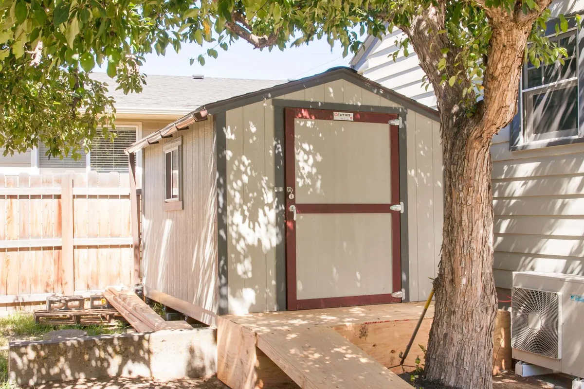 A practical backyard scene featuring a sturdy storage shed beneath leafy trees and beside a fenced yard. The shed is tidy and secure, providing a safe spot for storing bikes or outdoor gear after a day exploring Bend’s trails.