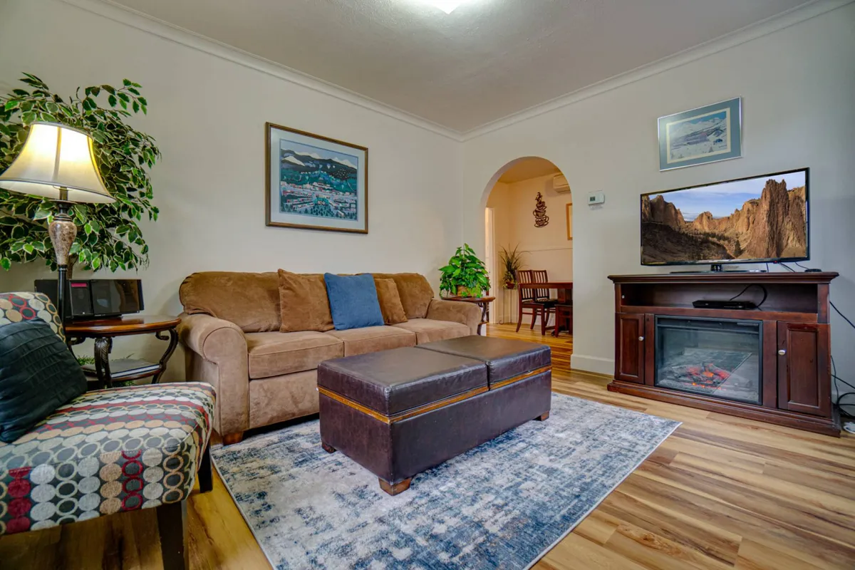 This image features a cozy living room with a plush sofa, a stylish coffee table, a television, lush green plant accents, and tasteful artwork. Natural light pours in from the large windows, illuminating the comfortable and inviting space. The overall atmosphere is warm and perfect for socializing or relaxing after a busy day.