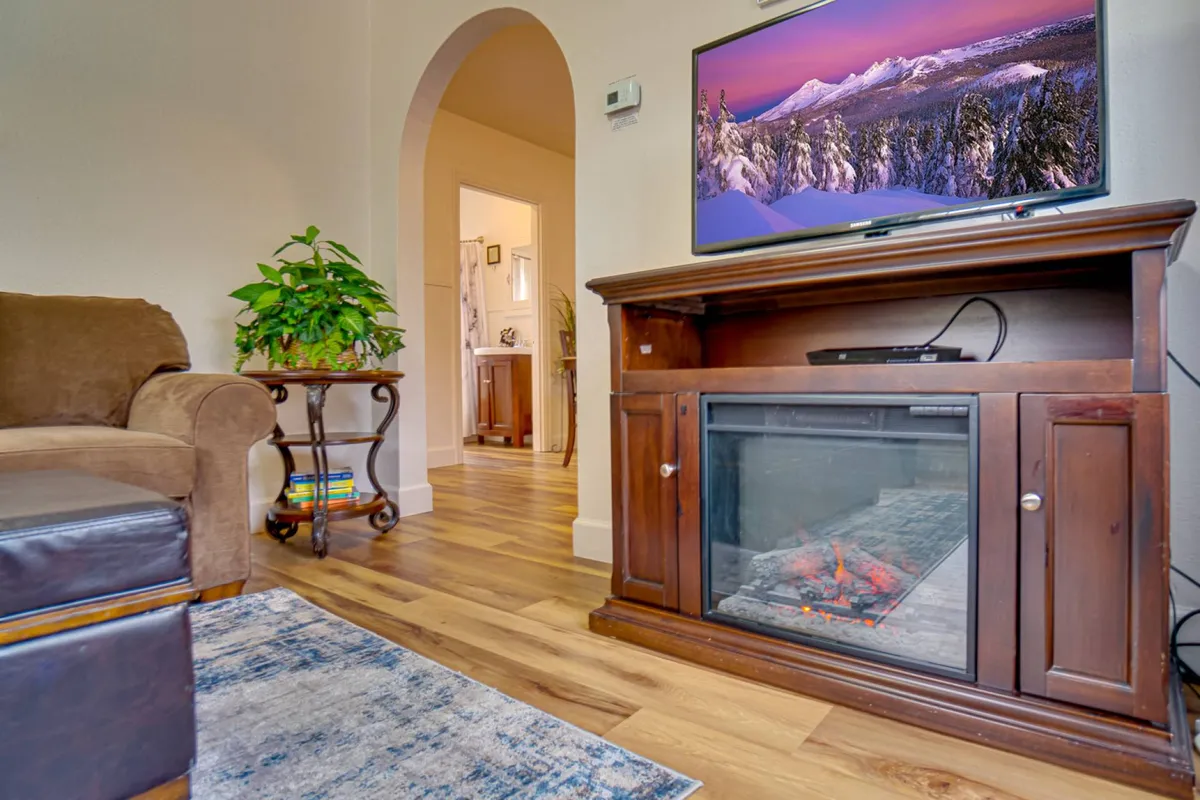 A warmly lit living room centered around a modern infrared fireplace, flanked by a comfortable sofa and a television. The space feels intimate and welcoming, ideal for cozy evenings spent relaxing by the fire or catching up on favorite shows.