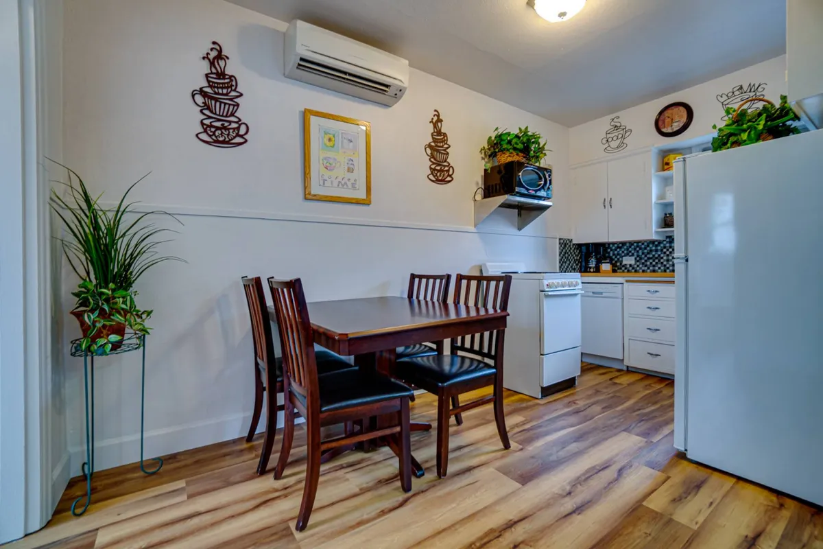 A cozy kitchen and dining area with a family-friendly dining table, kitchen appliances, wall decorations, and lush plants. The setup invites group meals, recipe sharing, and memory-making. The welcoming mood is perfect for both everyday and special occasions.
