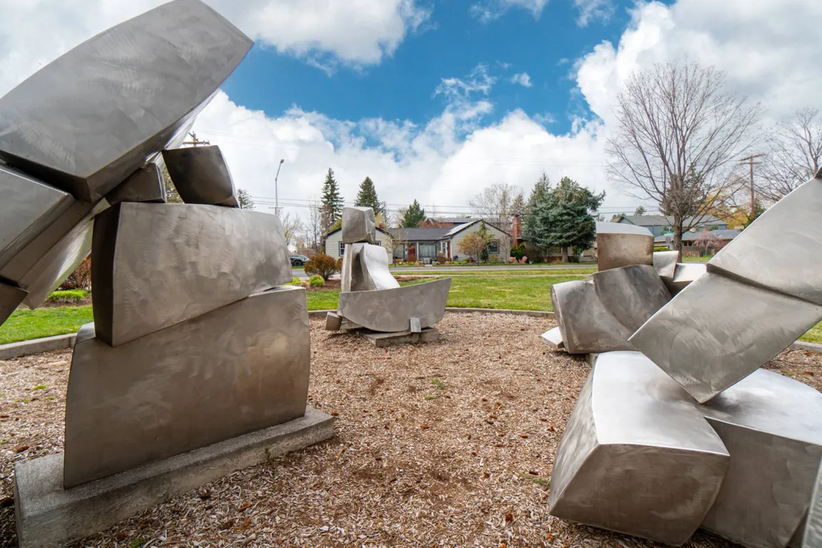 A vibrant green park dotted with unique metal sculptures and open space, perfect for strolling, enjoying art, or relaxing with a coffee. The scene introduces the blend of nature and creativity available just steps from downtown.