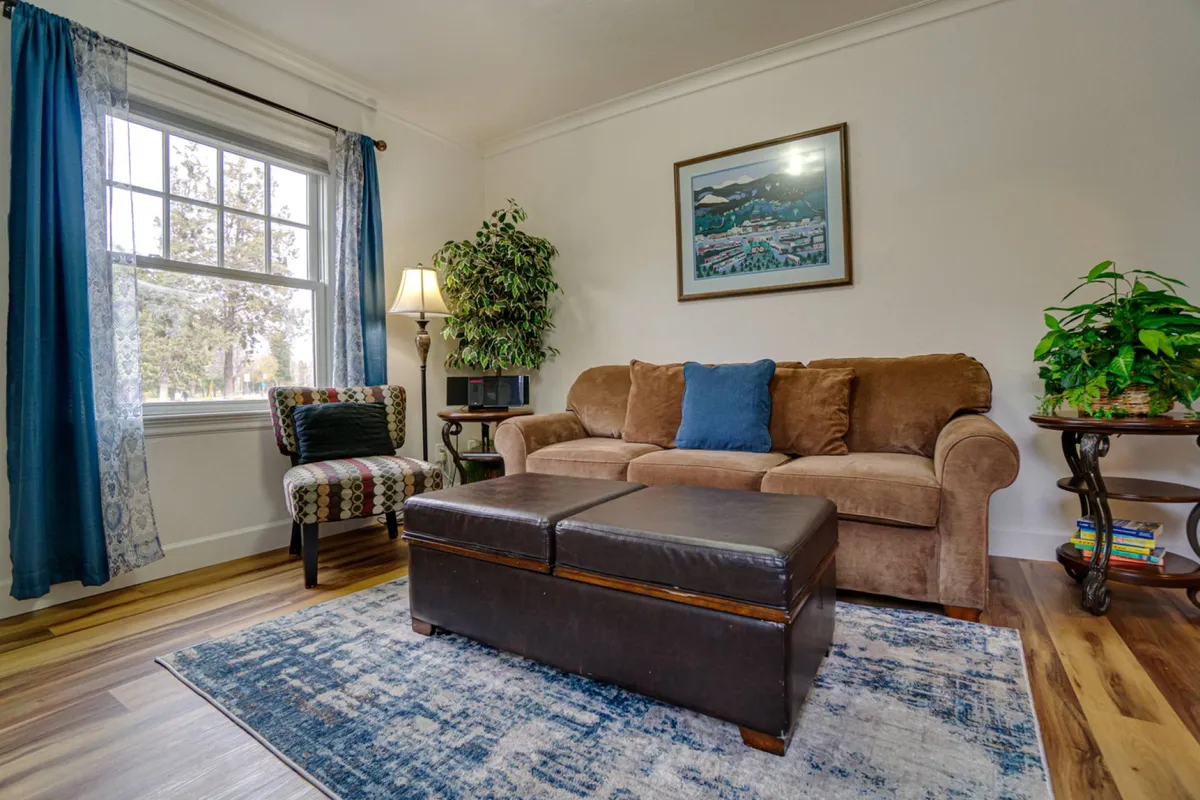 A bright living space with a comfortable sofa, a decorative chair, stylish artwork, a leafy indoor plant, and an accent table. Natural light streams in, creating a welcoming environment perfect for morning coffee or evening chats.